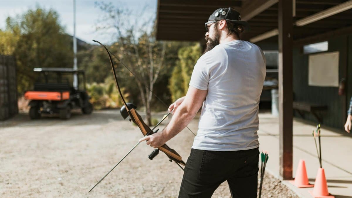 A man engages in archery practice outdoors on a sunny day.