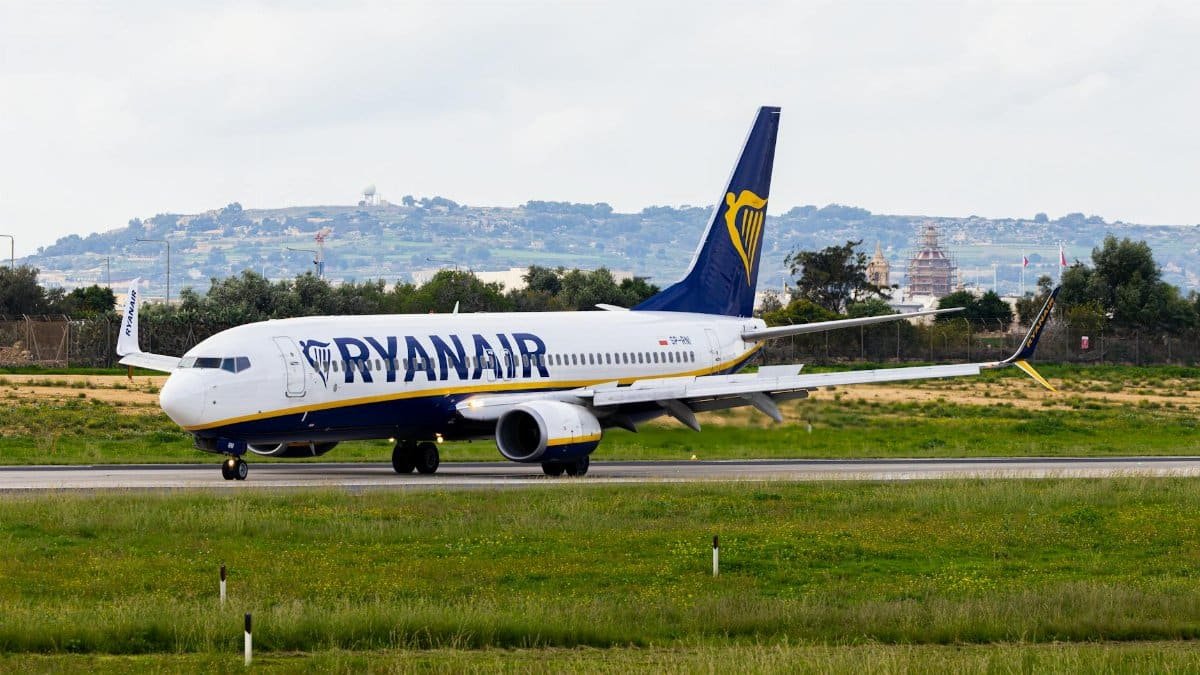 Ryanair airplane taxiing on runway with scenic hilly background.
