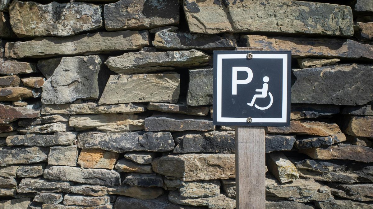 Outdoor accessible parking sign mounted on a rustic stone wall, sunny day.