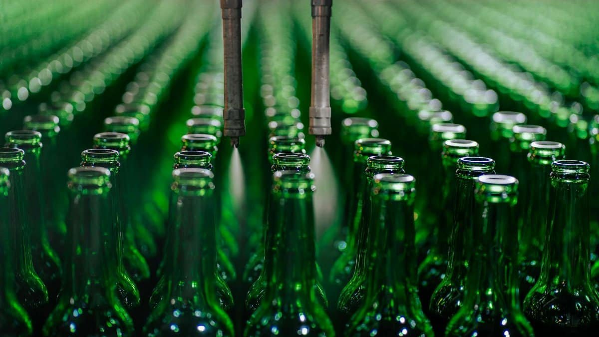 Rows of green glass bottles on an automated production line in a factory setting.