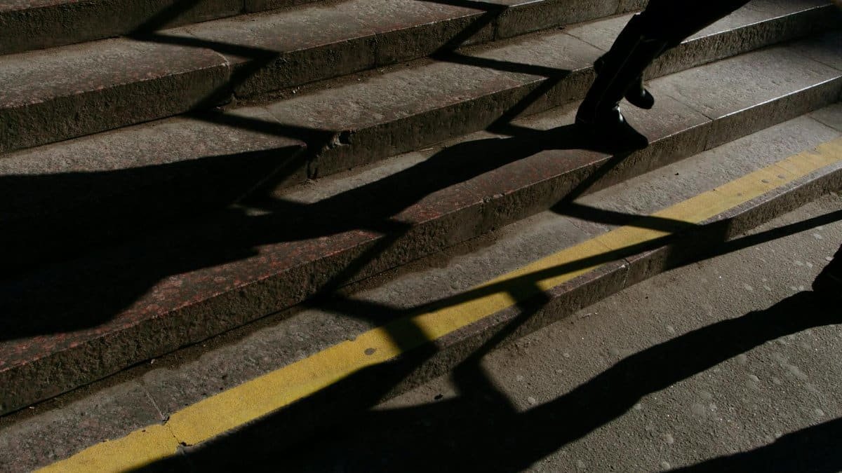 A person walks on stone steps with dramatic shadows and yellow line in sunlight.