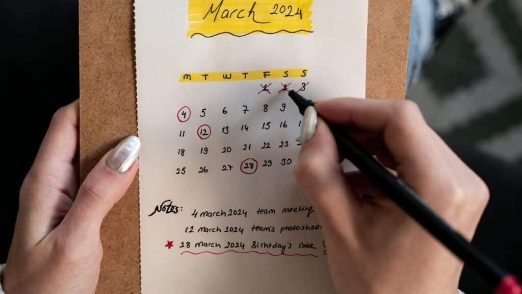Close-up of a woman's hands organizing a planner for March 2024 with handwritten notes and highlights.