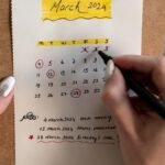 Close-up of a woman's hands organizing a planner for March 2024 with handwritten notes and highlights.