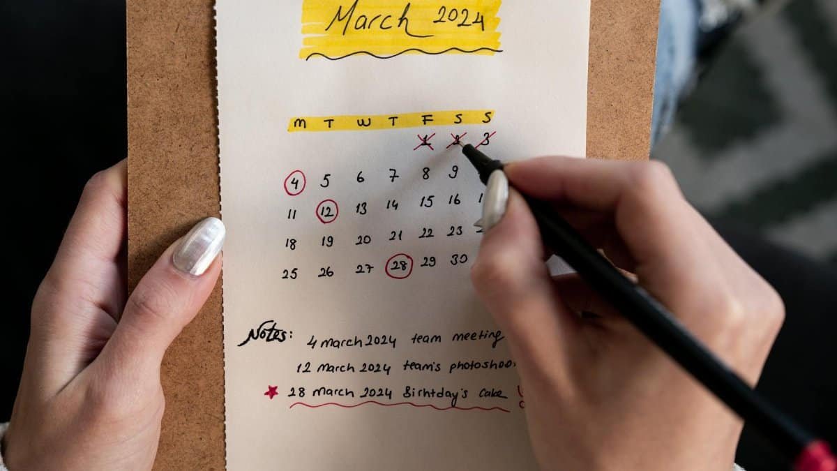 Close-up of a woman's hands organizing a planner for March 2024 with handwritten notes and highlights.