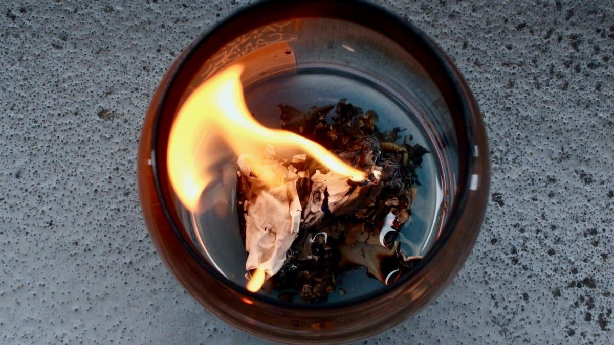 A close-up of paper burning inside a glass container showing a fiery flame.
