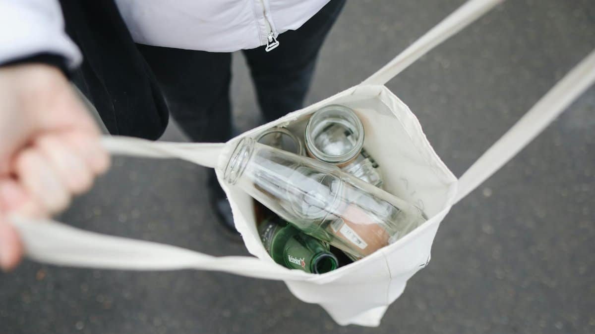 Person carrying a tote bag filled with glass bottles for recycling, promoting sustainability.