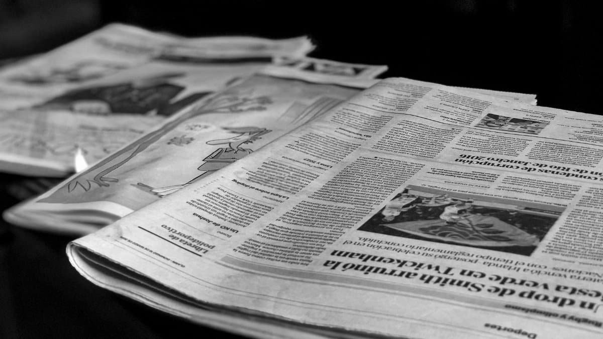 Black and white close-up image of newspapers laid on a table, emphasizing print media.