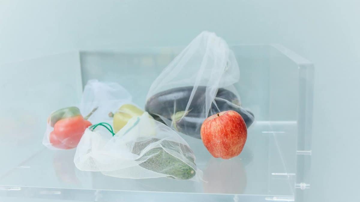 Reusable produce bags filled with fresh vegetables and a red apple, promoting eco-friendly shopping.