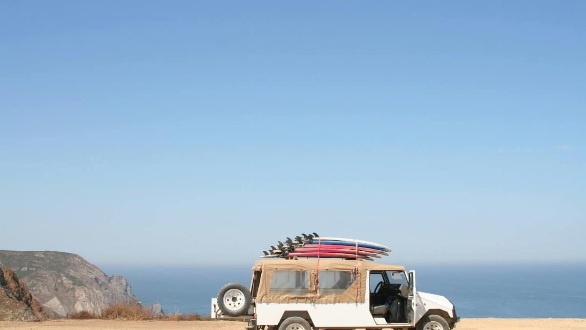 A jeep loaded with surfboards parked by a scenic ocean cliff under a clear sky.