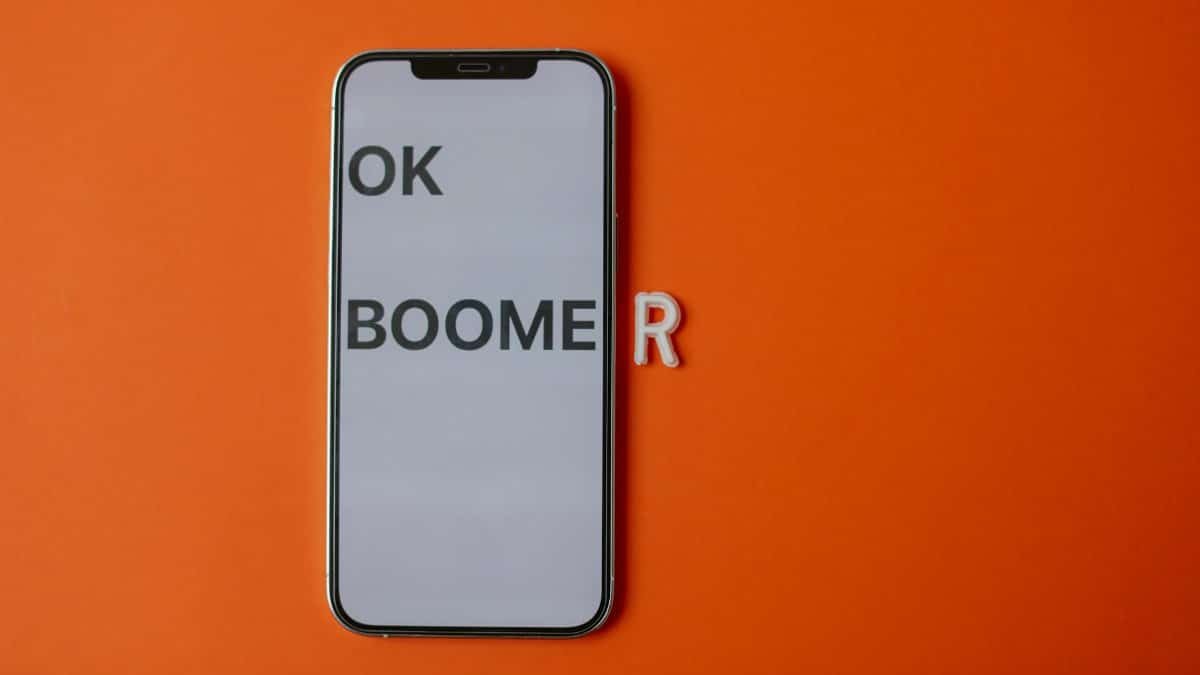Modern smartphone displaying 'OK Boomer' on orange backdrop, symbolizing generational divide.