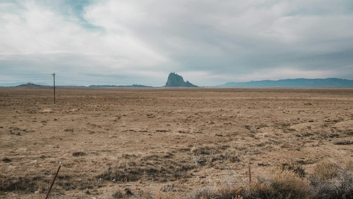 Expansive desert view of Shiprock in New Mexico, USA, under a cloudy sky.