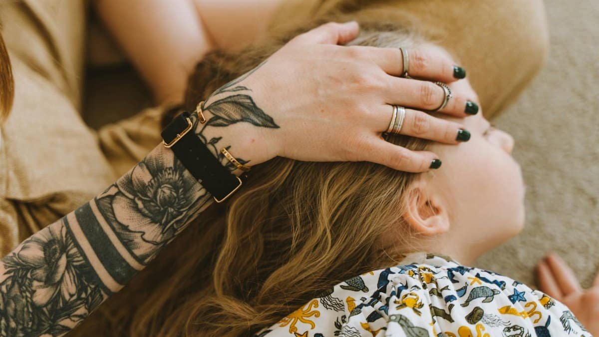 Close-up of a mother's tattooed hand gently comforting her child in a warm moment.