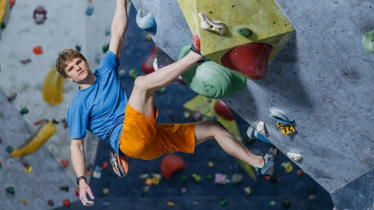 An athletic man skillfully climbing an indoor bouldering gym wall, showcasing rock climbing techniques.