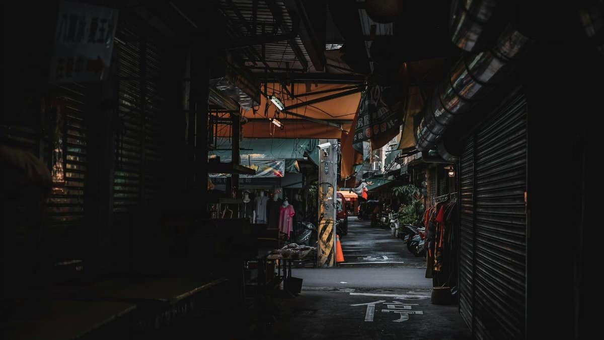 A dimly lit urban street market at twilight with closed shops and moody atmosphere.