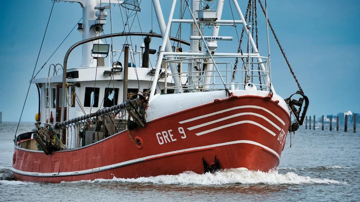 Red fishing trawler navigating calm waters under a clear blue sky.