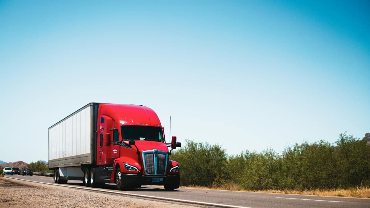 Vibrant red semi-trailer truck driving on an open highway under a clear blue sky.