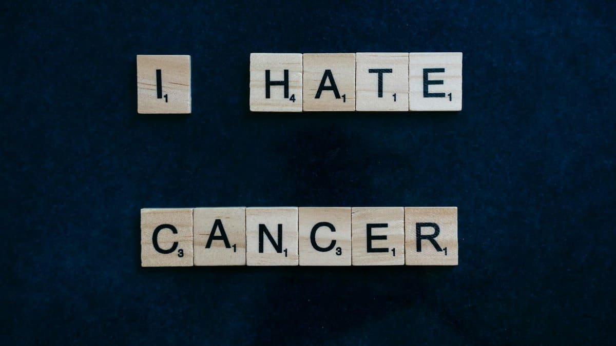 Wooden Scrabble tiles on a blue background, sharing a cancer awareness message.