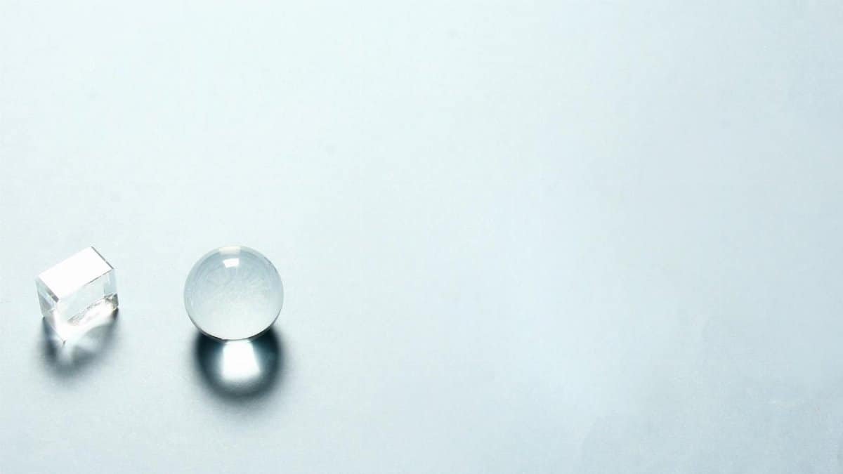Minimalist composition with a transparent crystal sphere and cube casting shadows on a light background.