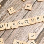 Close-up of wooden letter tiles on a table spelling 'Discovery', representing exploration and creativity.