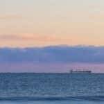 Tranquil ocean view at sunset in New Plymouth, Taranaki, New Zealand with a distant cargo ship.