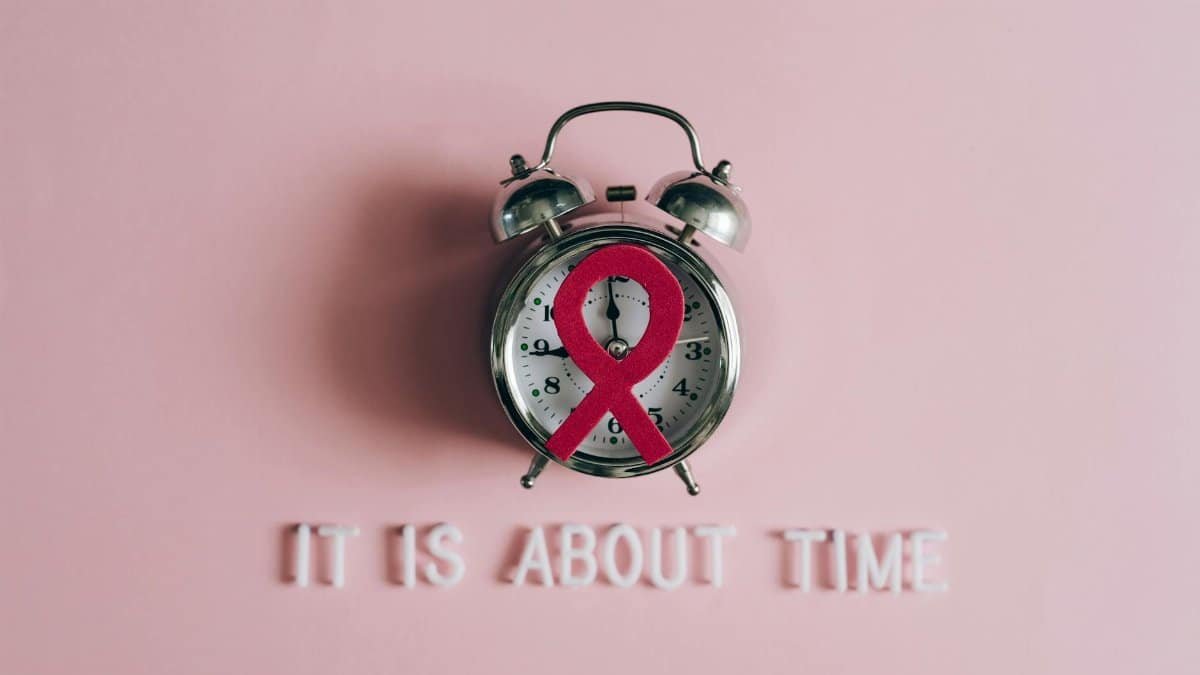 Alarm clock featuring an AIDS awareness ribbon on a pink background, symbolizing urgency and awareness.