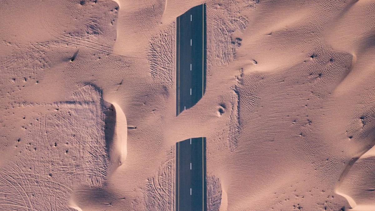 Aerial photograph of a highway cutting through vast sand dunes in a desert landscape.