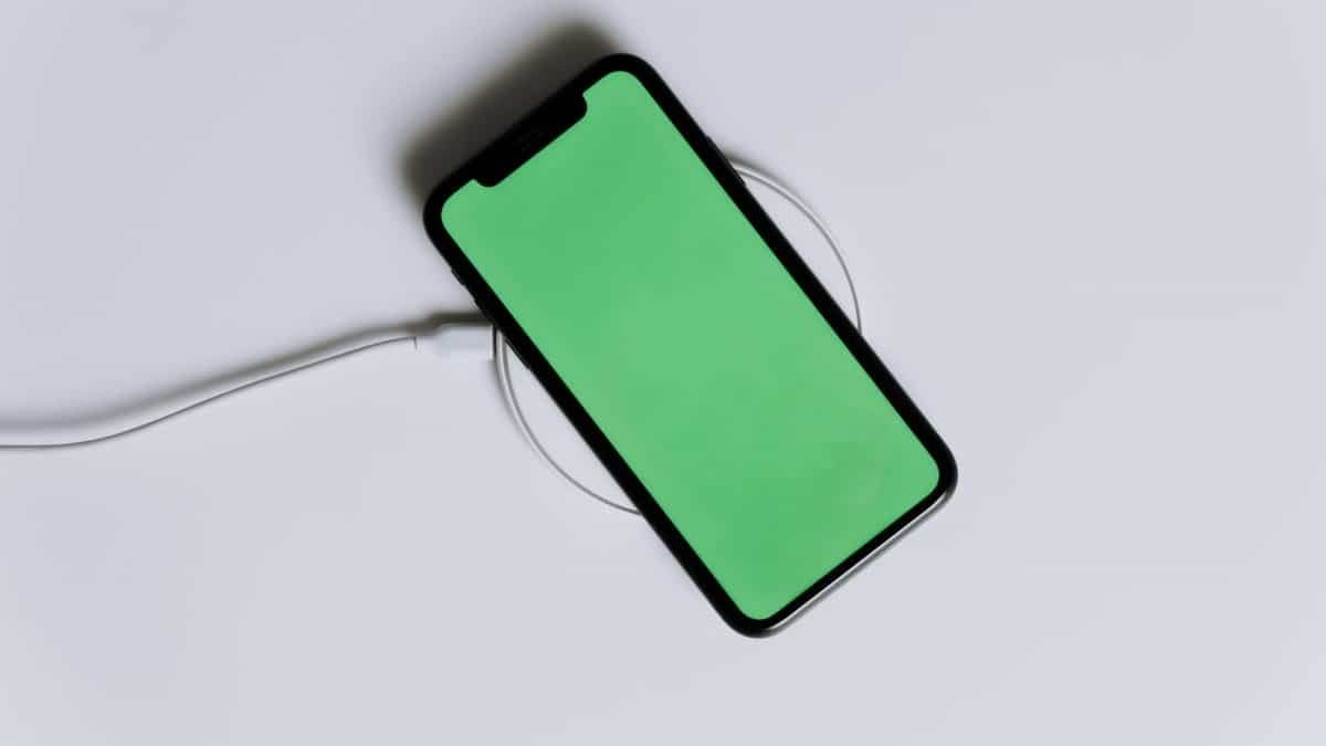 A minimalist smartphone with a green screen on a wireless charger, ideal for tech mockups.