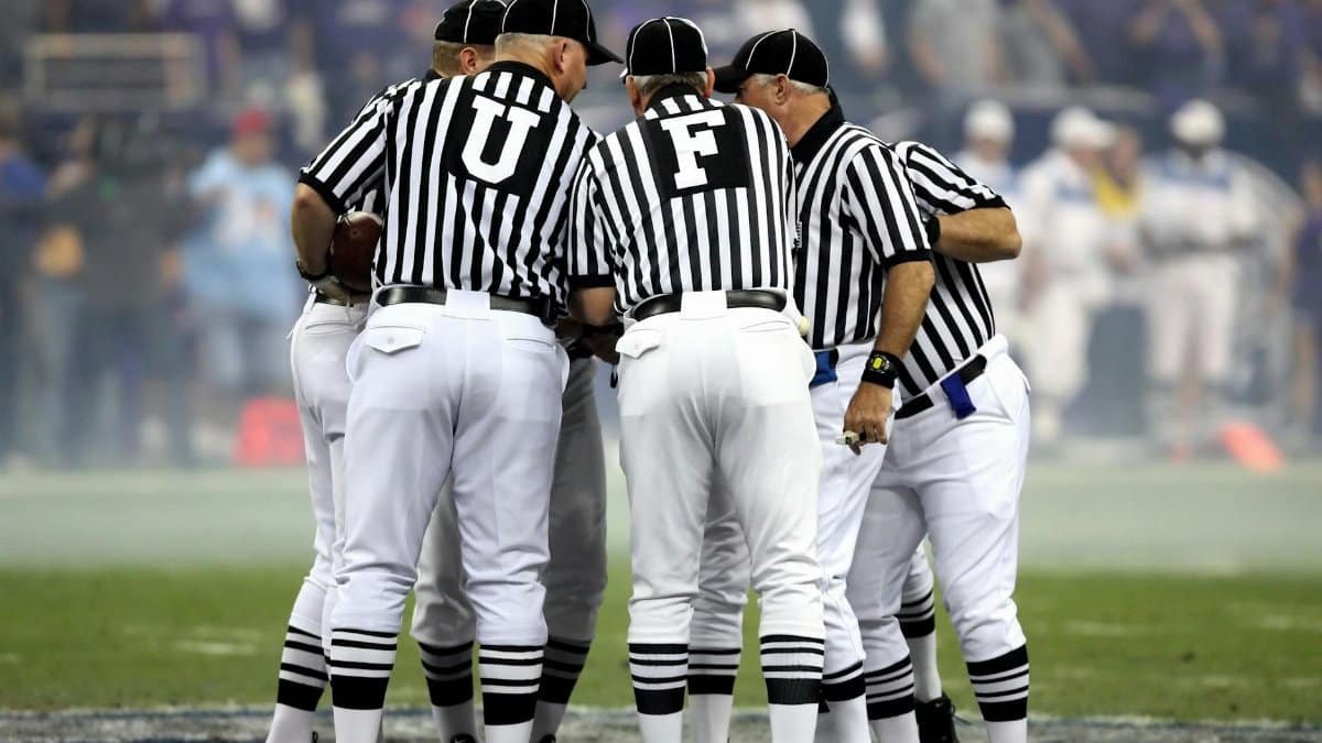 Group of sports officials in striped uniforms discussing on a football field.