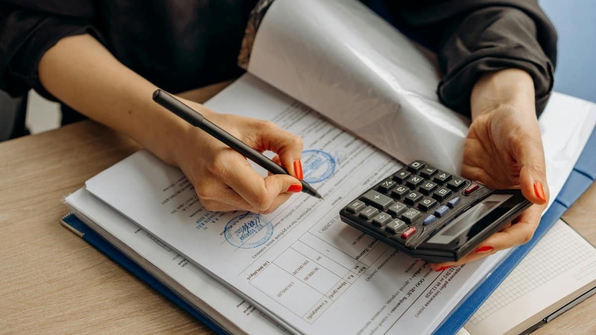 An accountant using a calculator and signing paperwork, showcasing financial analysis.