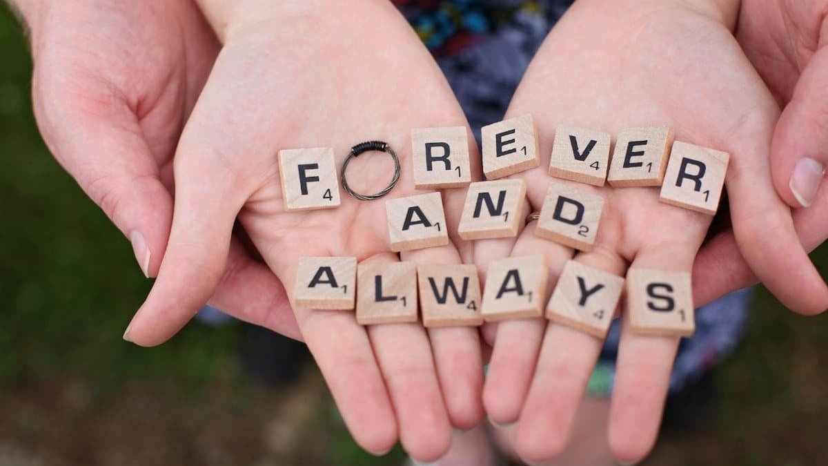 Hands holding 'forever and always' in Scrabble letters, symbolizing eternal love.