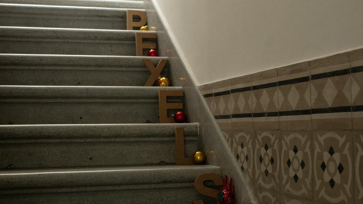 Wooden letters spelling 'Pexels' on stone stairs decorated with holiday ornaments.