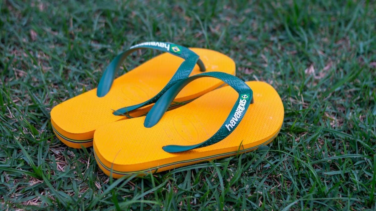 Close-up of yellow and green flip flops on a lush grassy field outdoors, perfect for summer vibes.