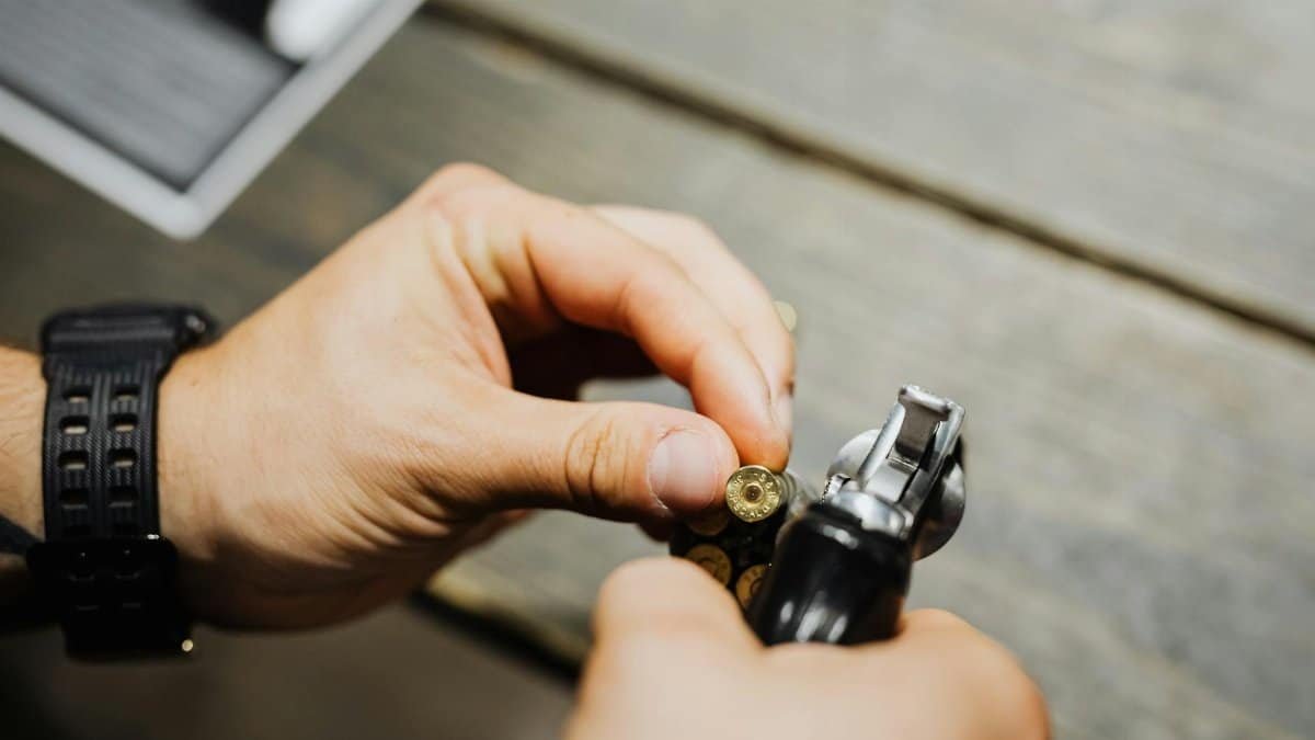 Close-up of hands loading bullets into a revolver on a wooden surface.