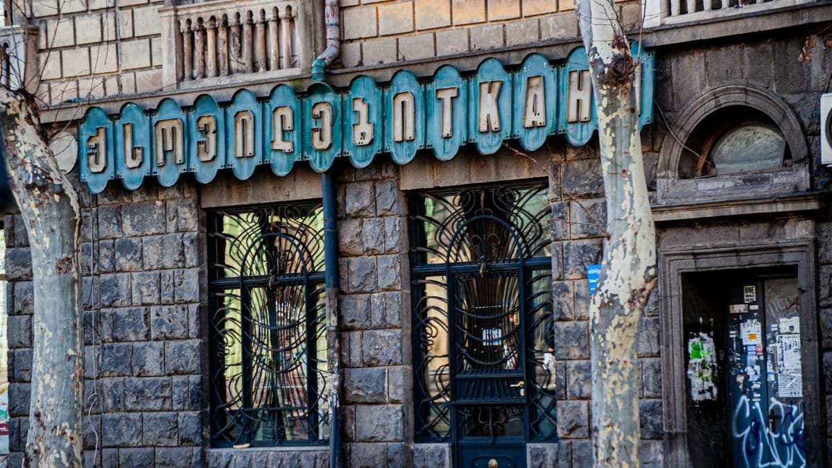 Elegant stone building facade with vintage style lettering and ironwork details, showcasing urban architecture.