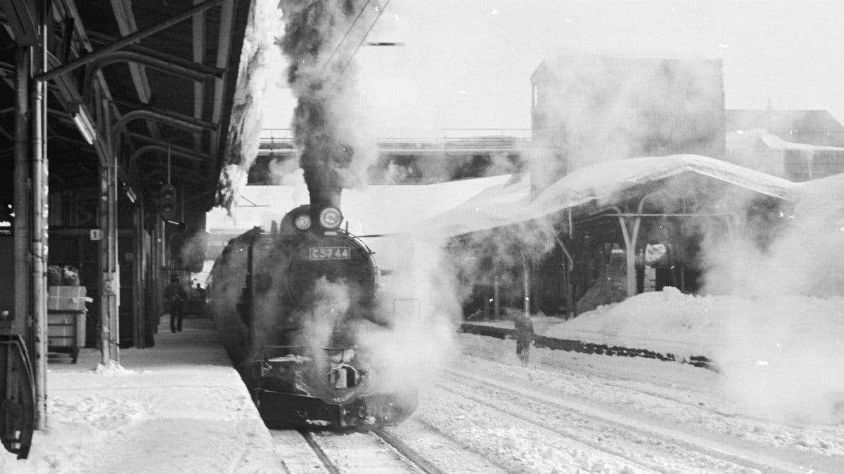 Black and white photo of a steam locomotive at a snowy train station filled with smoke.