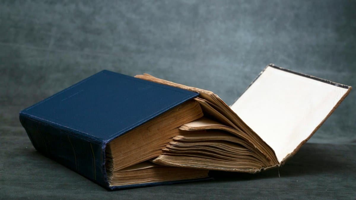 A worn-out vintage book with blue hardcover resting open on a dark surface, displaying aged pages.