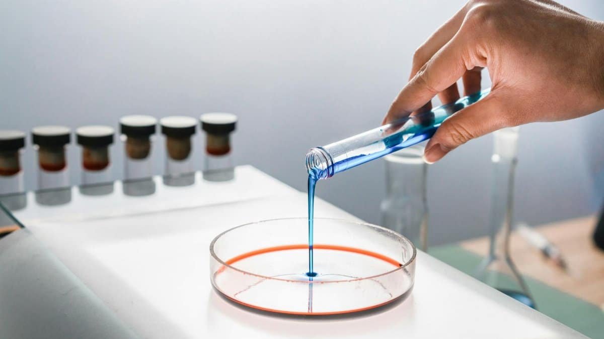 Scientist pouring blue liquid into a petri dish in a laboratory setting, focusing on research and experimentation.