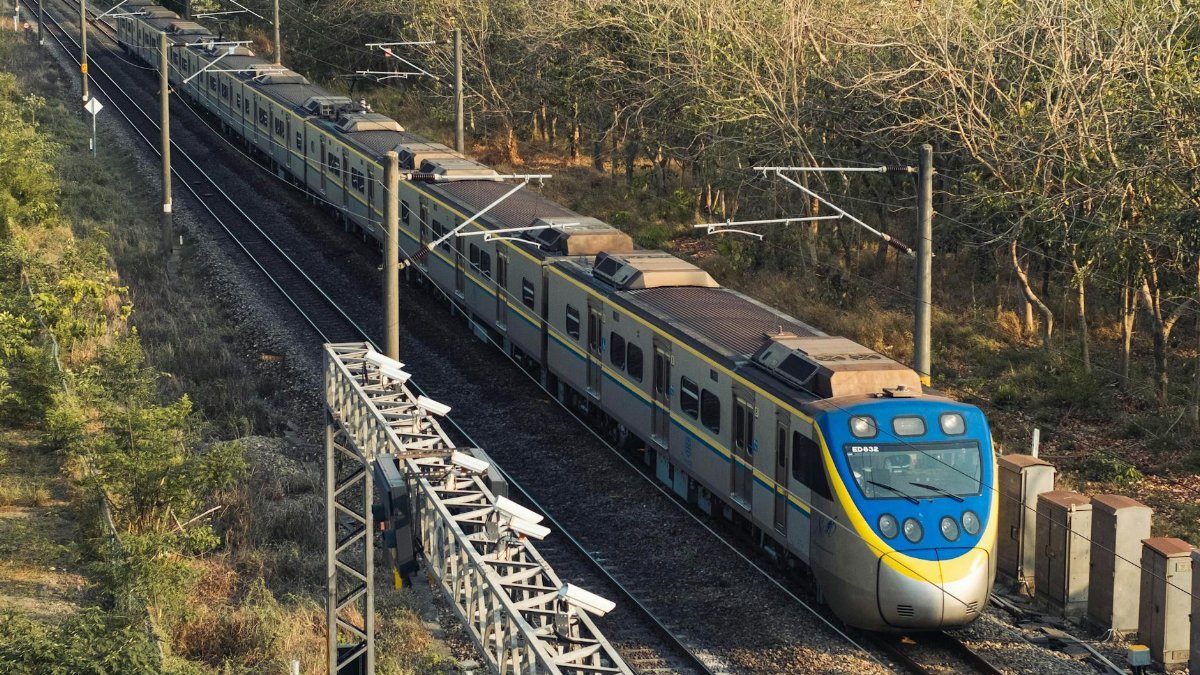 A passenger train travels through a wooded landscape captured from above.