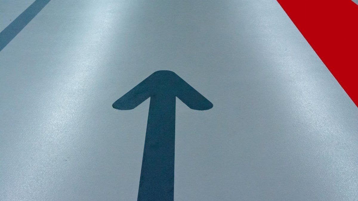 Blue arrow and red line on a parking garage floor signify direction and order.