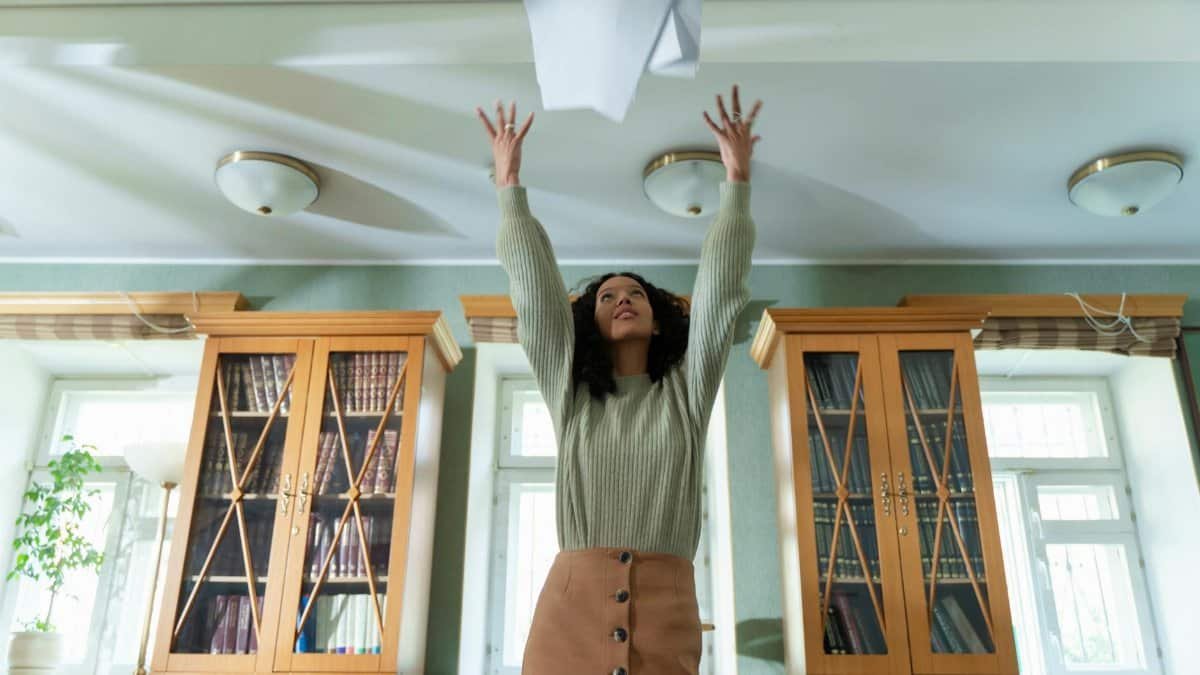 A young woman throws papers in the air in a library, expressing joy and relief.
