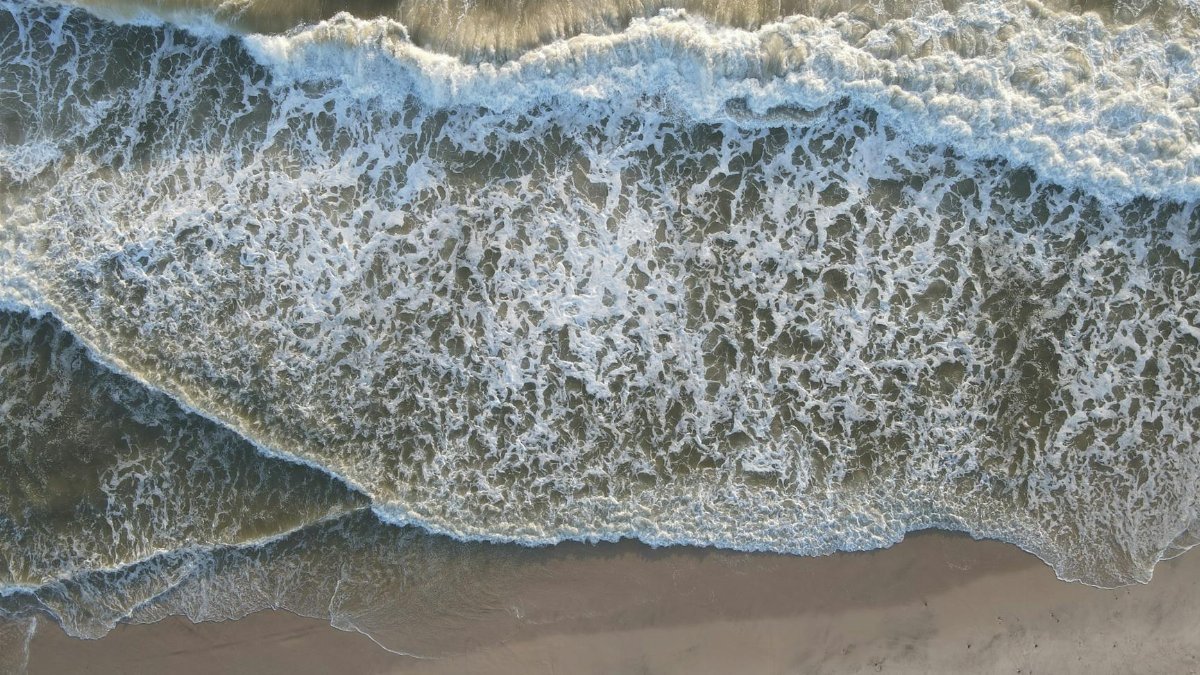Stunning aerial view of ocean waves crashing onto the sandy shores of Hvide Sande, Denmark.