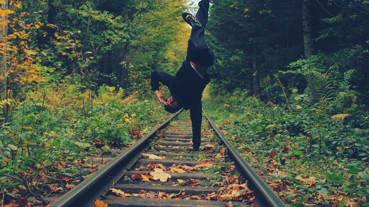 A man does a handstand on a railway track surrounded by vibrant autumn forest foliage.
