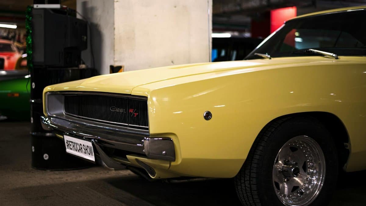 A sleek yellow Dodge Charger R/T showcased at a retro car exhibition indoors.