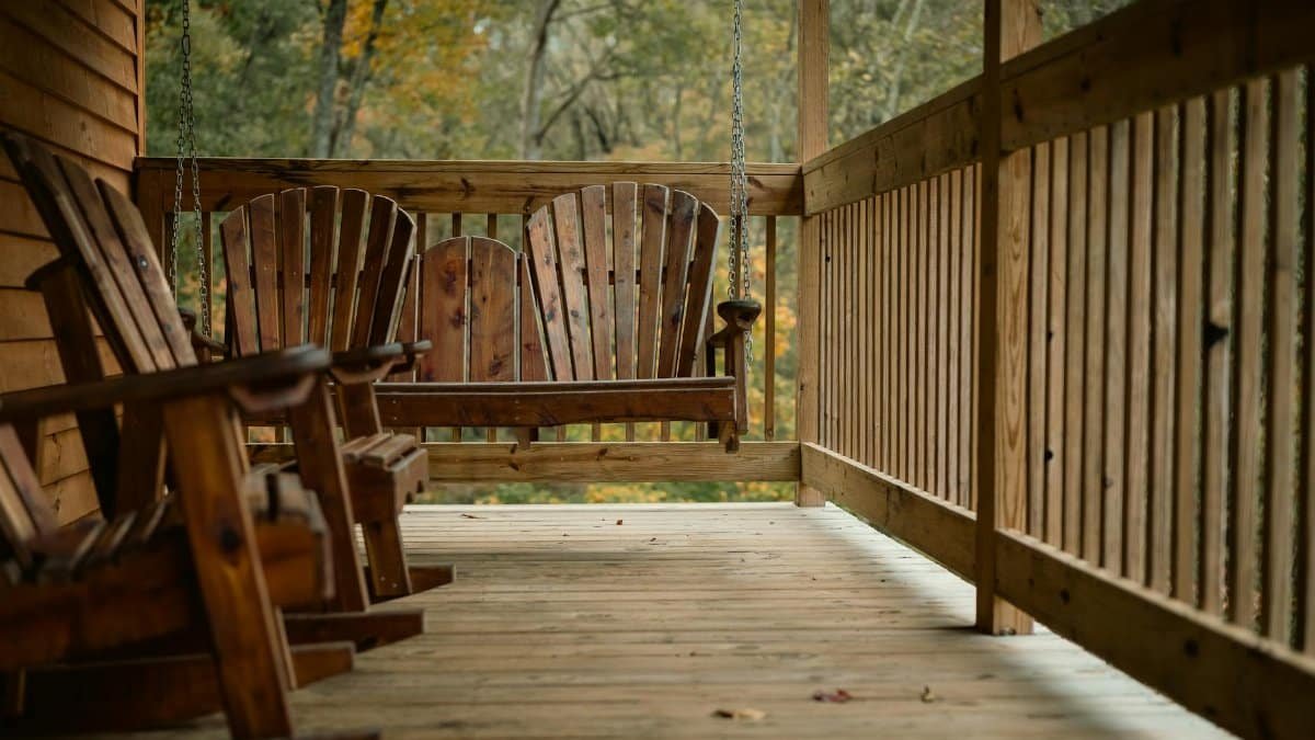 A serene wooden porch featuring a rustic hanging swing amidst autumnal foliage.