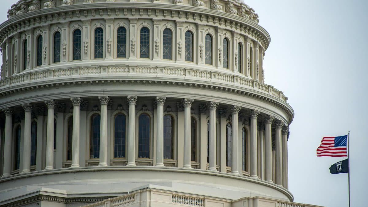 Detail of the US Capitol dome in Washington, D.C., featuring an American flag waving beside it.