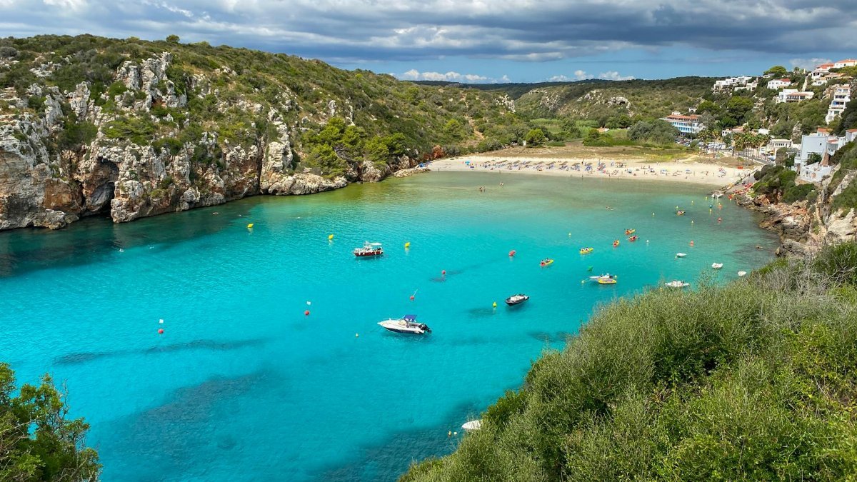 Stunning aerial shot of the vibrant Cala en Porter beach in Menorca, showcasing turquoise waters and rugged cliffs.