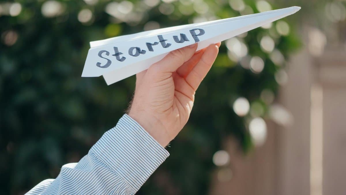 Close-up of a hand holding a paper plane with 'Startup' written, symbolizing a business launch.