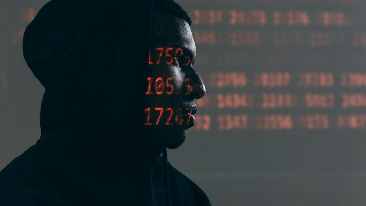Side profile of a man in a hoodie, surrounded by red code, depicting cybersecurity theme.