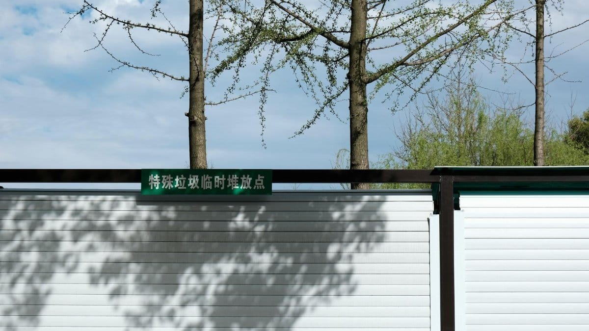A metal fence casting shadows with trees in the background under a clear sky.