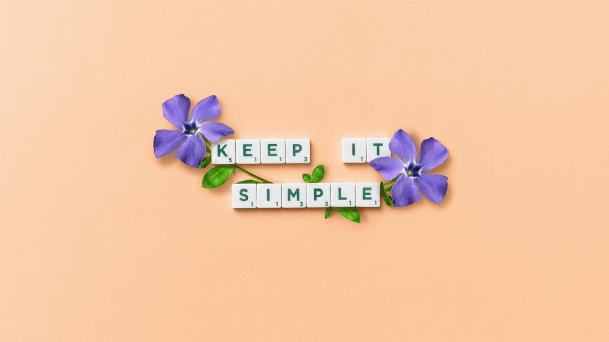 Scrabble tiles spell out 'Keep It Simple' with purple flowers on a pastel background.